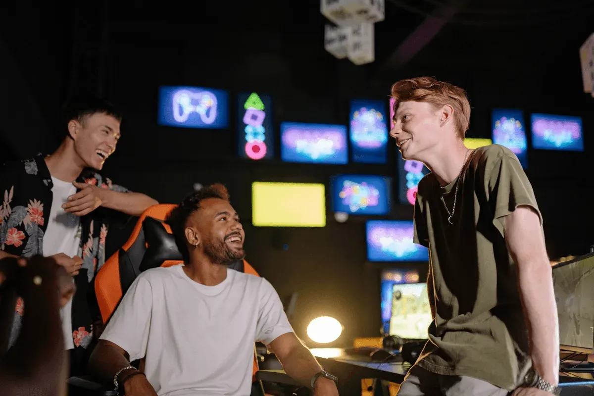 Three friends laughing together in an arcade lined with neon game screens