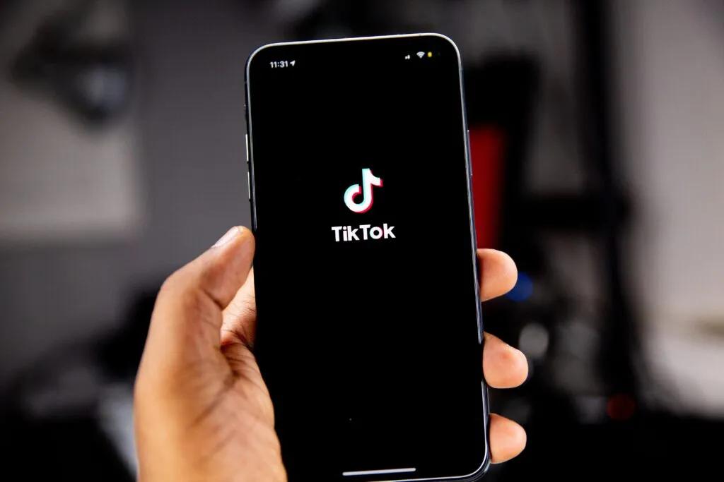 Hand holding a smartphone showing the TikTok logo on a black startup screen